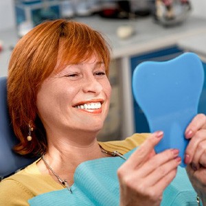 Woman in the patient’s chair smiling in a small mirror