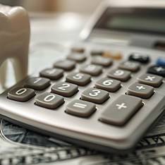 Model tooth next to calculator on top of dollar bills