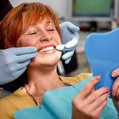 A senior woman admiring her dental implants in a hand mirror