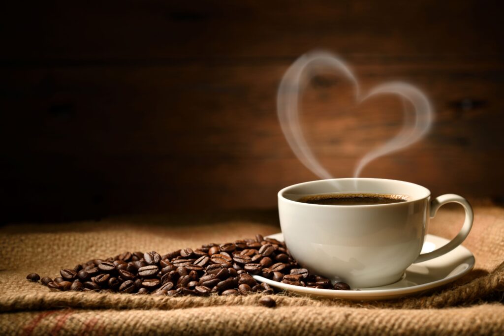 Cup of coffee with steam making a heart on tweed next to coffee beans